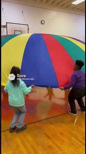 Kids in gym class holding and lifting a large, colorful parachute during a classic parachute game