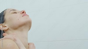 Close up woman standing under streams of cool water and enjoying process of taking shower in white shower in bathroom. Concept of young woman standing under streams of clean water.