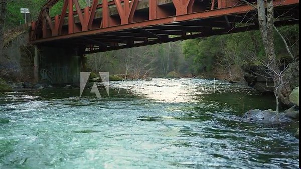 Rushing creek flowing underneath an old bridge within Lassen National Forest during a light breeze