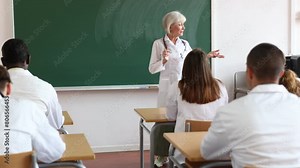 Senior woman professor explaining subject to group of medical students and colleagues in university.