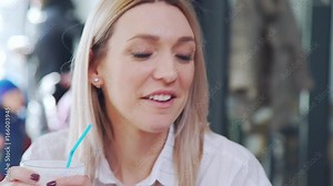 Young blonde woman talking, laughing and drinking milkshake. At a meeting with her friends: a beautiful blonde is talking to the other person. Working group meeting, business breakfast