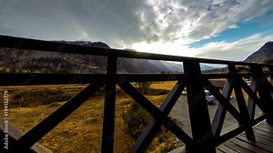 4K UHD time lapse of wooden fence on high terrace at mountain landscape with clouds and sun rays. Autumn or winter weather. Horizontal movement on motorised slider dolly.