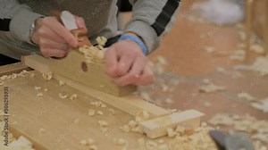 Slow motion: man carpenter using spokeshave or plane to shape and smooth woodboard on workbench at workshop - close up view. Design, carpentry, craftsmanship and handwork concept