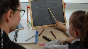 Preschool teacher teaching child alphabet. Preschool girl learning alphabet letters, using chalkboard.