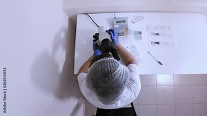 Woman laboratory assistant in the workplace for a microscope in the laboratory conducts research of biological material, standing next to the test tubes and special documents for records, top view