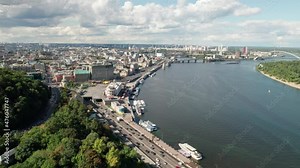 Aerial view of the metropolis by the river with skyscrapers and car traffic. Panoramic view of the cityscape near nature parks in summer. Kyiv. Industrialization. Flight in the big city.