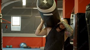 A man bodybuilder carrying the punching bag on the shoulder and puts it down