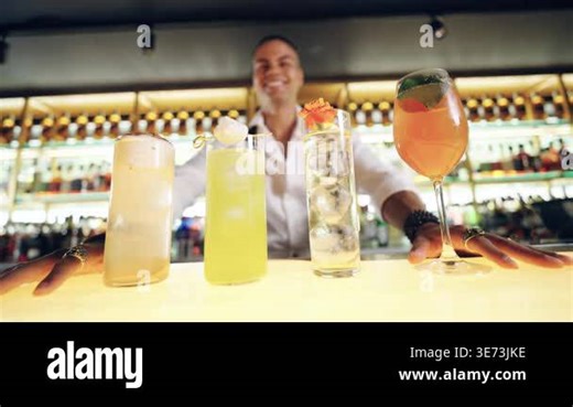 Friendly smiling bartender proudly showing a selection of refreshing and creative alcoholic beverages lined up on an illuminated bar counter Stock Video Footage - Alamy