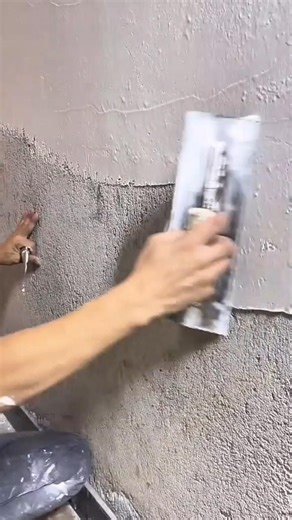 applying several grey cement layers on an indoor wall surface using a professional manual hand tool