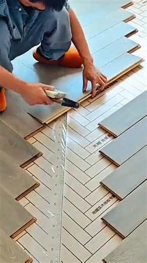 installing gray wooden floor planks in a chevron pattern using a hammer on a white subfloor