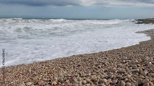 Continuous ocean waves drench a sandy and rocky beach, suitable for use as a dynamic vacation background in creative projects.