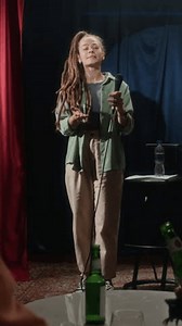 Vertical shot of audience watching Caucasian female show host with dreadlocks announcing entrance of red-haired stand-up artist on stage who taking seat and starting speech