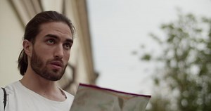 Male traveler scratching temple while looking for direction on map