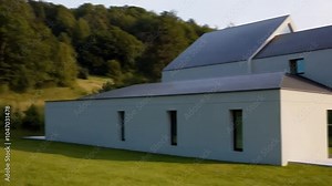 A beautiful modern farmhouse with a light gray exterior and a sleek charcoal roof, nestled in a green grassy landscape. The home�s minimalist design contrasts with the vibrant surroundings.