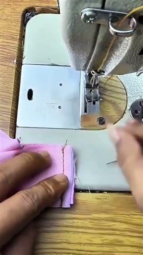 sewing a light pink fabric precisely using a professional industrial machine in a garment workshop