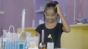 Confused girl kid scratching head by looking lab equipments at chemistry laboratory while making experiment - concept of difficulty in learning at school.