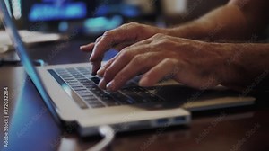 Two hands typing and using the trackpad in a laptop computer. Close up shot with blurred background.