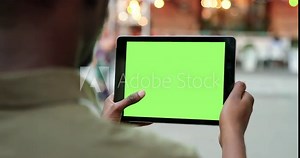 Male hands holding tablet with green screen. Guy using mobile phone while walking in the autumn street. Back view shot. Chroma key, close up man hand holding device with vertical green screen