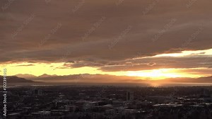Sun rays shining through clouds over Utah Lake past Provo city during sunset.