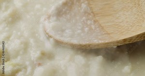 Close video of heating canned clam chowder with a wood spoon on the food.