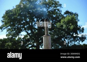 Farm tractor exhaust pipe releasing light smoke under clear blue sky and green trees. Engine emissions and mild air pollution often associated with older farm equipment. . High quality 4k footage