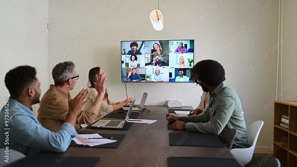 A team actively engages with remote colleagues via a large screen, illustrating the modern hybrid work model where technology bridges the gap between in-office and remote team members