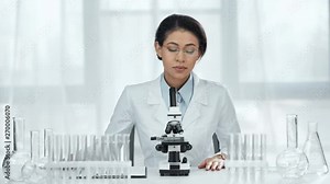 african american scientist sitting on chair and looking at sample through microscope in lab
