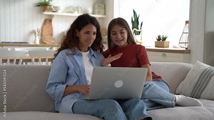 Friendly Caucasian woman and teen girl of school age make videocall in laptop and waving hand. Positive mother and daughter are recording online video on computer webcam sits on couch in own home