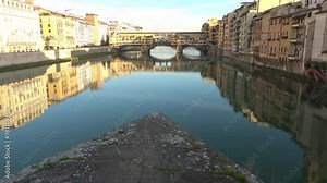The Ponte Vecchio, old segmental arch bridge with stores and housing over the Arno River, in Florence, Italy. Golden reflections on water
