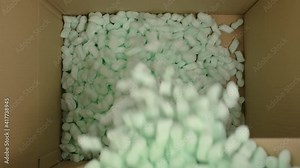 Storyfoam Packing peanuts being poured falling into cardboard box, care shipping products for customers by packaging starch protective granules . Online shopping retailer