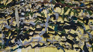 The camouflage net for military lies on the floor. A net of pieces of cloth helps soldiers to hide from the enemy during the war. The net is woven by volunteer people who want to help their defenders.