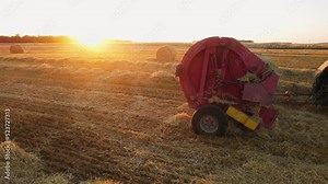 Agricultural machine making hay bale make round large bales. Haymaking. Hay making machine at sunset. Tractor collecting hay and making haystacks.