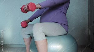 A pregnant girl goes in for sports with dumbbells and sits on a fitball ball. The concept of sport during pregnancy and health.