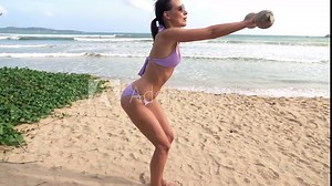 Young woman in bikini doing squats with dumbbells on beach, super slow motion 240fps