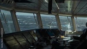 Storm in ocean. Navigation bridge of ship inside. Control panel in foreground. Strong pitching. Sea view from wheelhouse windows. Foam on high waves.