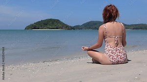 Young pretty woman back view sitting in meditation position on the beach