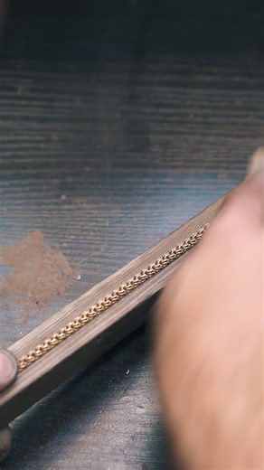 CU: experienced goldsmith polishes new shining bracelet with rasp on wooden gutter at dark table in workshop close view | Premium Stock Video Footage