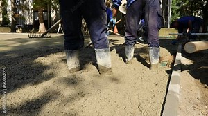 Construction workers, riggers are using rake to spreading, leveling concrete covering square reinforcement, pouring layer of concrete in foundation.