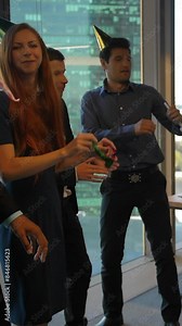 Happy colleagues celebrating birthday at the modern coworking office. Serpentine, pipes. Daylight, smiles and dancing in holiday caps. Slow Motion. Vertical shot.