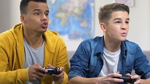 Two male friends winning in video game, sitting on couch, teenage friendship