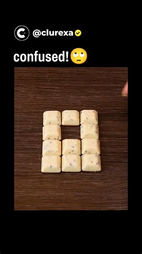 Clurexa on Instagram: "The post features a 16-second video of a woman rapidly assembling small white chocolate squares into Tetris-like shapes on a wooden surface, captioned "confused!" to feign bewilderment at the seamless process. Close inspection reveals a sleight-of-hand trick at around 5 seconds, where she conceals and inserts an extra 12th piece behind her hand, turning an impossible puzzle into a solvable one. With over 2.4 million views and 783 replies, the thread sparks humorous debunki