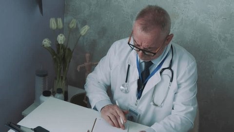 clip-4002612773-elderly-male-physician-stethoscope-writing-on-notepad