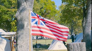 Video View of the Grand Union flag and the United States. First American flag waving in the wind on a bright autumn day at a park with fall landscape
