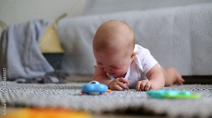 Cute baby girl having tummy time on the floor and crying for attention, being surrounding with toys, learning to control her head, early development.