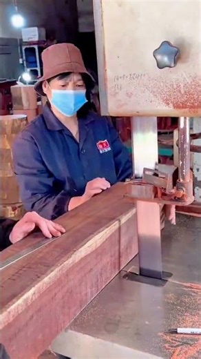 Two masked workers using a vertical bandsaw to cut thick wood