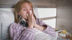 Beautiful sick woman lying on bed, suffering from flu or coronavirus symptoms. Adult ill female coughing and taking a pill with water as having a temperature.