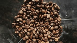 Electric coffee grinder working process, beans are jumps up and then milled and explodes in pentagon glass bowl, top view