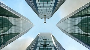 Airplane flying over skyscrapers and reflects in glass modern facades. High rise city centre corporate buildings.