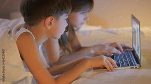Children play on the computer in the bed under the blanket at night. Computer games.