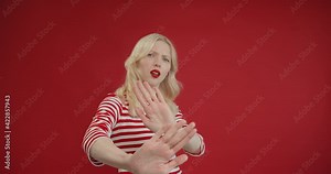 Dissatisfied woman showing stop sign with outstretched hand and saying don't show me this, deny reject concept on red background
